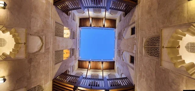 منظر داخلي متناظر في حصن جبرين بسلطنة عمان يظهر العمارة العمانية التقليدية والأقواس الخشبية حول الفناء الداخلي.
