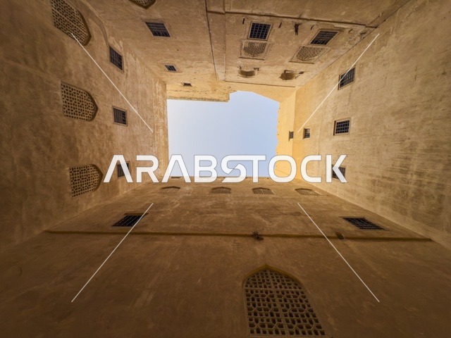 منظر داخلي متناظر في حصن جبرين بسلطنة عمان يظهر العمارة العمانية التقليدية والأقواس الخشبية حول الفناء الداخلي.