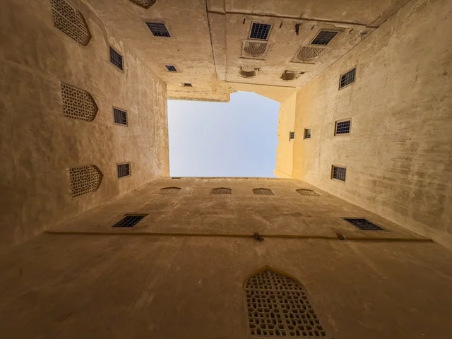 منظر داخلي متناظر في حصن جبرين بسلطنة عمان يظهر العمارة العمانية التقليدية والأقواس الخشبية حول الفناء الداخلي.