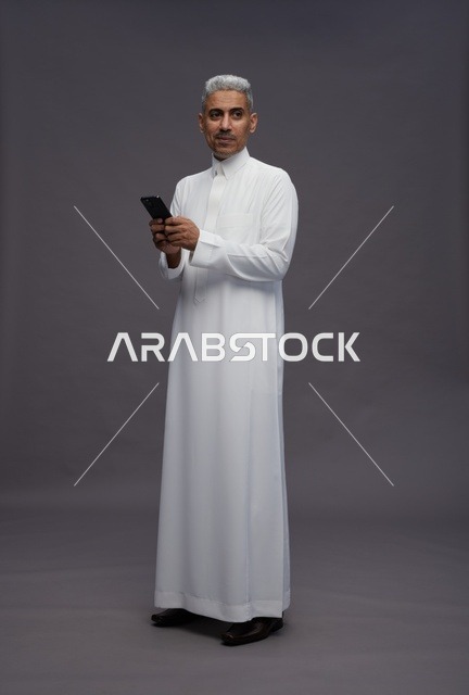رجل سعودي بالثوب التقليدي يستخدم الهاتف الذكي