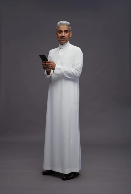 رجل سعودي بالثوب التقليدي يستخدم الهاتف الذكي