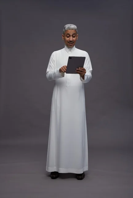 رجل سعودي بالزي التقليدي يستخدم جهاز لوحي