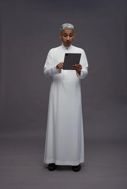 رجل سعودي بالثوب مع جهاز لوحي بخلفية رمادية