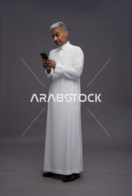 رجل سعودي بالزي التقليدي يستخدم هاتف ذكي