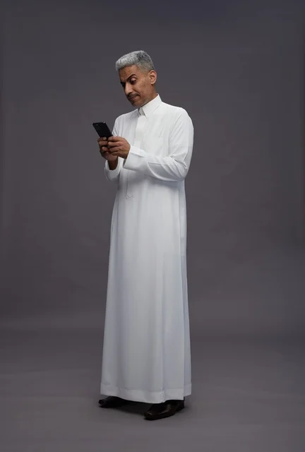 رجل سعودي بالزي التقليدي يستخدم هاتف ذكي