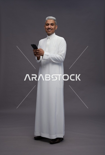 رجل سعودي بالثوب التقليدي يستخدم الهاتف الذكي