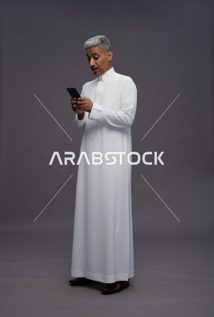 رجل سعودي بالثوب الأبيض يستخدم هاتف ذكي في استوديو