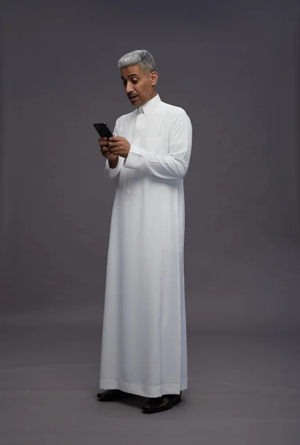 رجل سعودي بالثوب الأبيض يستخدم هاتف ذكي في استوديو