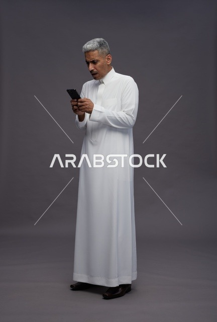 رجل سعودي بالثوب يستخدم الهاتف الذكي في الاستوديو