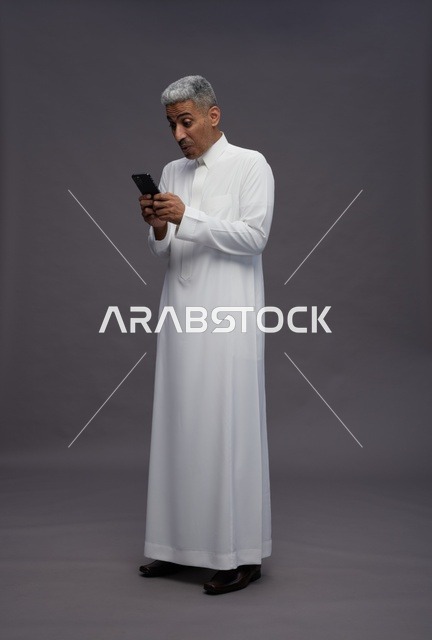 رجل سعودي بالزي التقليدي يستخدم الهاتف الذكي