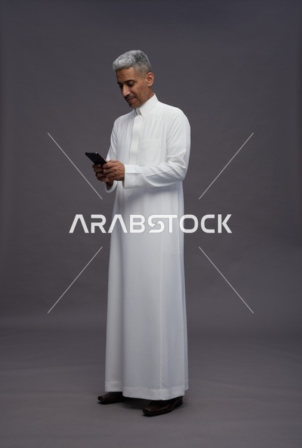Saudi Man in Thobe Using Smartphone on Grey Background