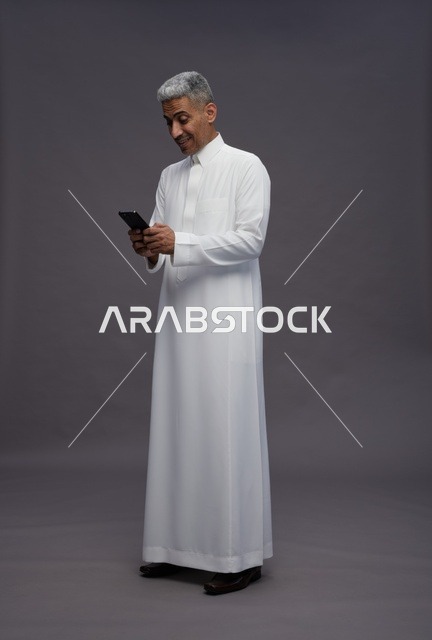 رجل سعودي بالثوب التقليدي يستخدم الهاتف الذكي