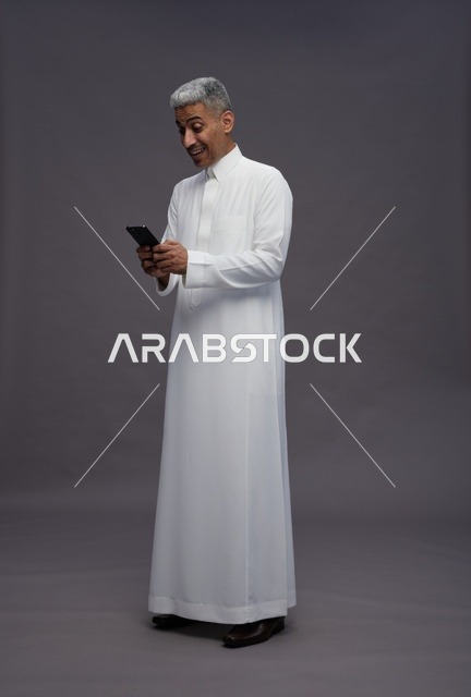 رجل سعودي بالزي التقليدي يستخدم هاتف ذكي في استوديو