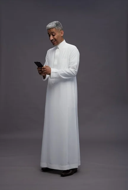 رجل سعودي بالزي التقليدي يستخدم هاتف ذكي في استوديو