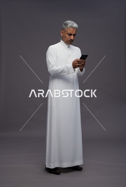 رجل سعودي بالزي التقليدي يستخدم الهاتف الذكي