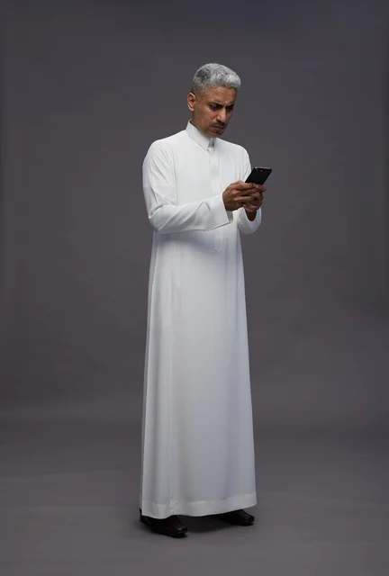 رجل سعودي بالزي التقليدي يستخدم الهاتف الذكي