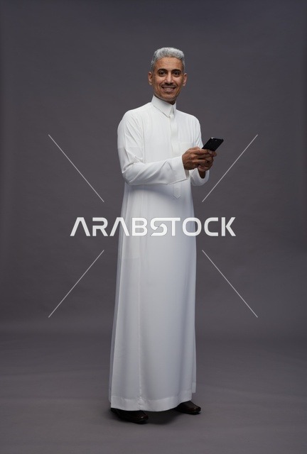 رجل سعودي بالثوب التقليدي يستخدم الهاتف الذكي