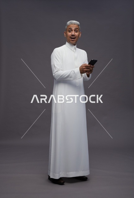 رجل سعودي بالزي التقليدي يستخدم هاتفاً ذكياً
