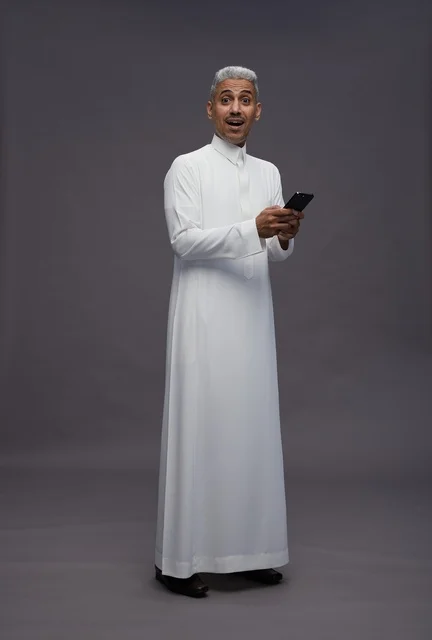 رجل سعودي بالزي التقليدي يستخدم هاتفاً ذكياً