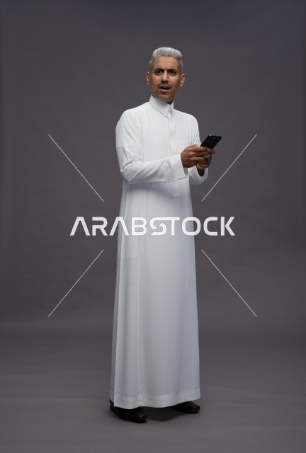 رجل سعودي بالزي التقليدي يحمل هاتف ذكي