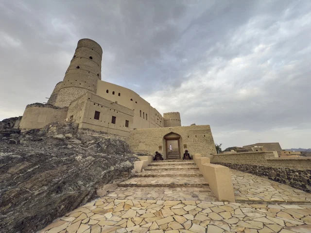 منظر لقلعة بهلا التاريخية في سلطنة عمان يظهر العمارة الطينية العريقة وأبراجها الدفاعية تحت سماء غائمة