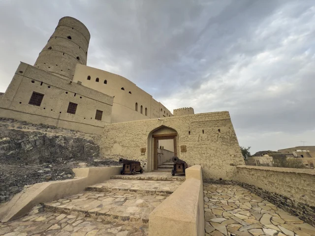 Bahla Fort in Oman showcasing its historic mud architecture and defensive towers under a dramatic cloudy sky. bahla.Oman  .