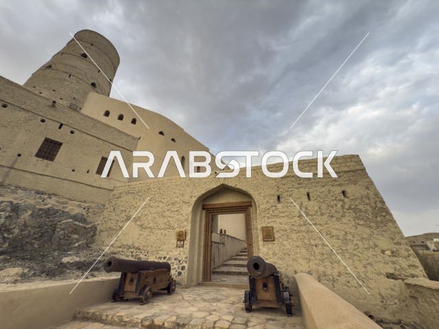 منظر لقلعة بهلا التاريخية في سلطنة عمان يظهر العمارة الطينية العريقة وأبراجها الدفاعية تحت سماء غائمة