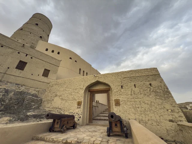 Bahla Fort in Oman showcasing its historic mud architecture and defensive towers under a dramatic cloudy sky. bahla.Oman  .