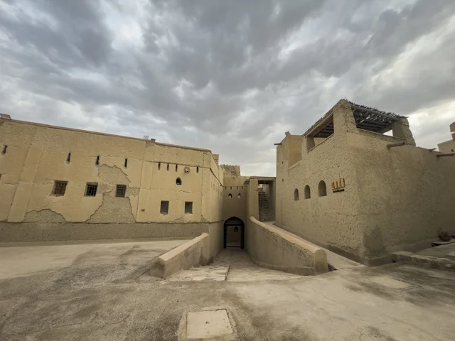 منظر لقلعة بهلا التاريخية في سلطنة عمان يظهر العمارة الطينية العريقة وأبراجها الدفاعية تحت سماء غائمة