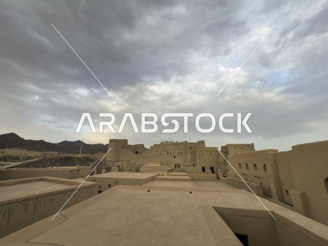 منظر لقلعة بهلا التاريخية في سلطنة عمان يظهر العمارة الطينية العريقة وأبراجها الدفاعية تحت سماء غائمة