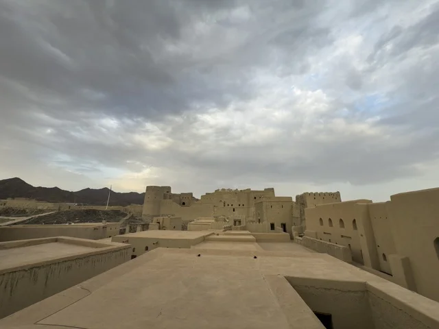 Bahla Fort in Oman showcasing its historic mud architecture and defensive towers under a dramatic cloudy sky. bahla.Oman  .