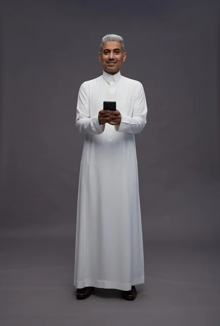 رجل سعودي يستخدم هاتفًا ذكيًا بالزي التقليدي