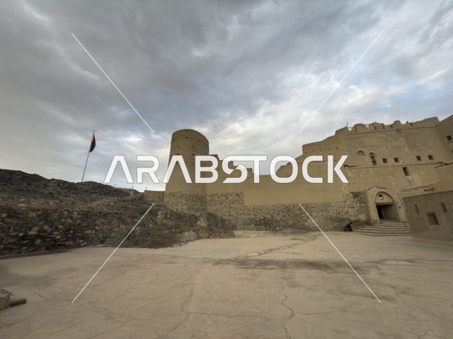 منظر لقلعة بهلا التاريخية في سلطنة عمان يظهر العمارة الطينية العريقة وأبراجها الدفاعية تحت سماء غائمة