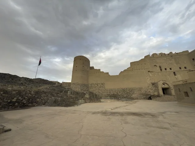 منظر لقلعة بهلا التاريخية في سلطنة عمان يظهر العمارة الطينية العريقة وأبراجها الدفاعية تحت سماء غائمة