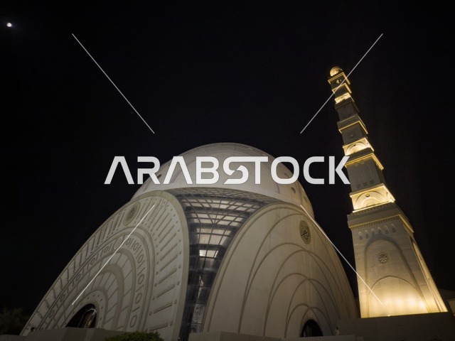 منظر ليلي لجامع الإسلام في مسقط يظهر القبة البيضاء والمئذنة المضيئة في أجواء روحانية هادئة