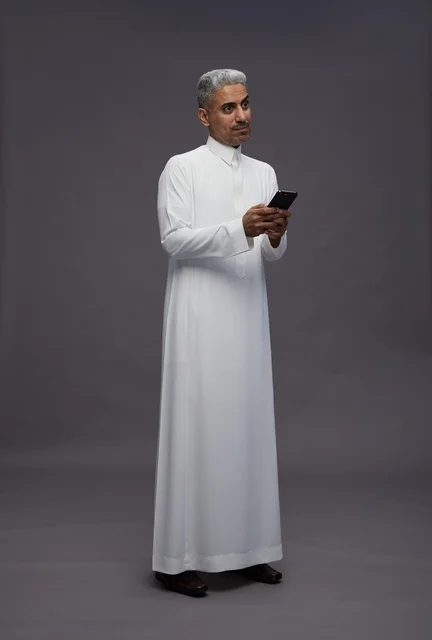 رجل سعودي بالثوب التقليدي يستخدم هاتف ذكي في استوديو