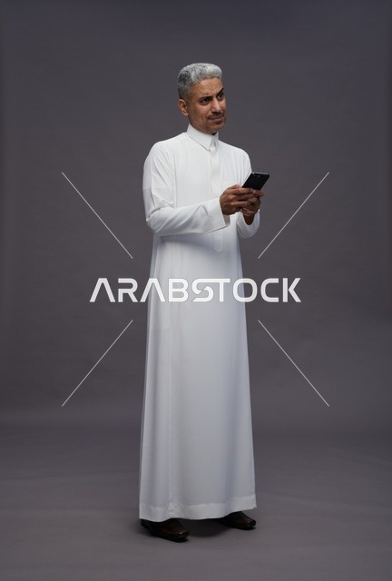 رجل سعودي بالثوب التقليدي يستخدم الهاتف الذكي في استوديو