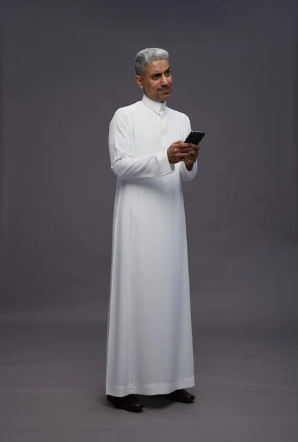 رجل سعودي بالثوب التقليدي يستخدم الهاتف الذكي في استوديو
