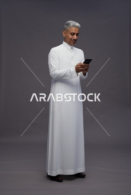 رجل سعودي بالثوب التقليدي يستخدم الهاتف الذكي