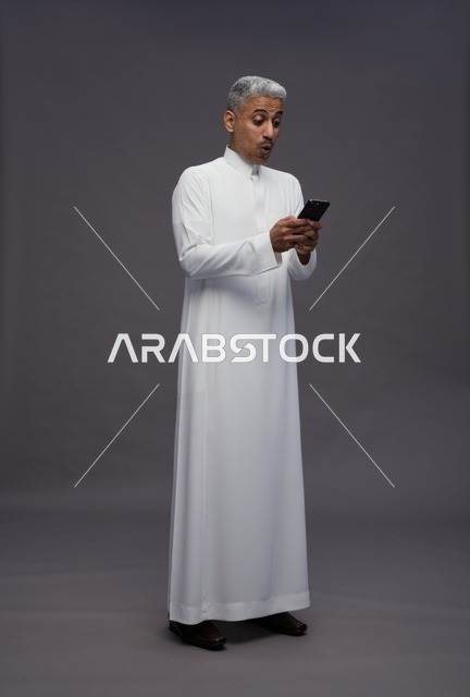 رجل سعودي بالثوب التقليدي ينظر للهاتف بتعجب
