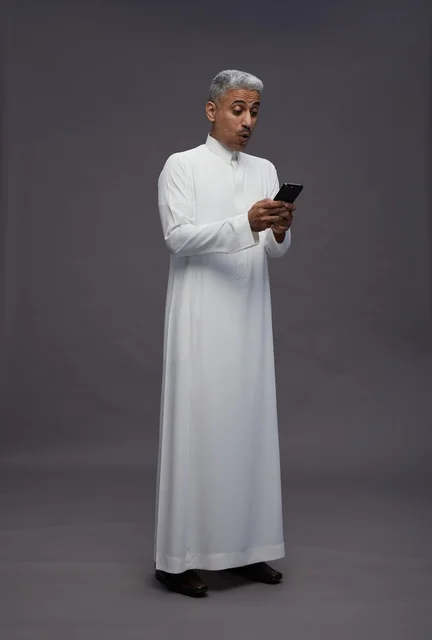 رجل سعودي بالثوب التقليدي ينظر للهاتف بتعجب