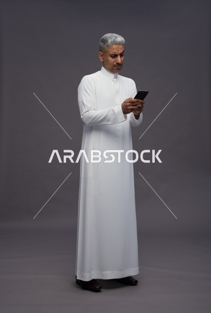 رجل سعودي بالزي التقليدي يستخدم الهاتف الذكي في استوديو