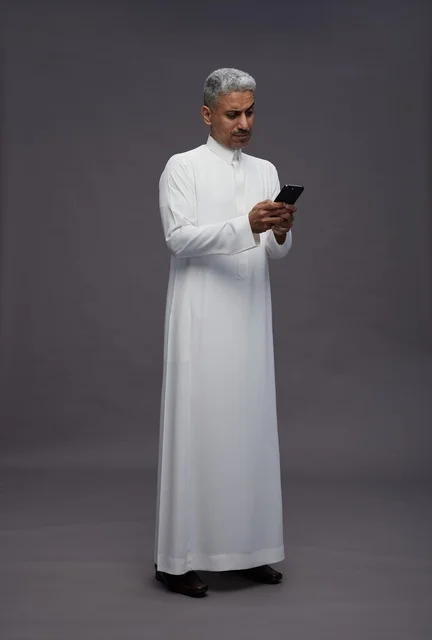 رجل سعودي بالزي التقليدي يستخدم الهاتف الذكي في استوديو