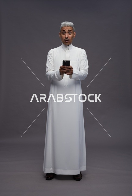 رجل سعودي بالثوب التقليدي يمسك هاتف ذكي