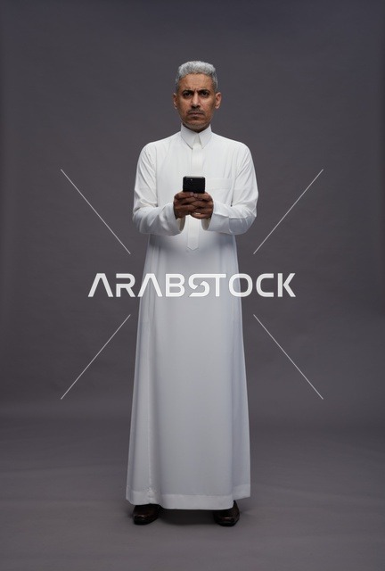 رجل سعودي بالثوب التقليدي يستخدم هاتف ذكي في الاستوديو