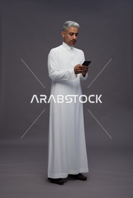 رجل سعودي بالزي التقليدي يستخدم الهاتف الذكي