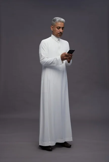 رجل سعودي بالزي التقليدي يستخدم الهاتف الذكي