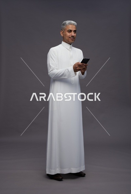 رجل سعودي بالثوب التقليدي يستخدم الهاتف الذكي