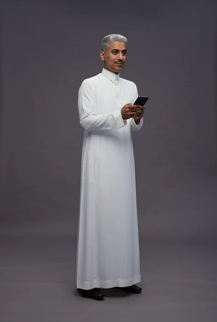 رجل سعودي بالثوب التقليدي يستخدم الهاتف الذكي