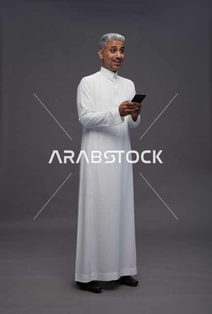 رجل سعودي يستخدم هاتف ذكي بالثوب التقليدي في استوديو
